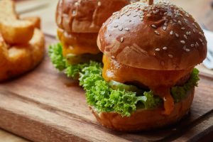 Close-up of juicy cheeseburgers with lettuce and pickles served on a wooden board.