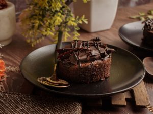 Rich homemade chocolate brownie served elegantly on a black plate with a gold spoon.